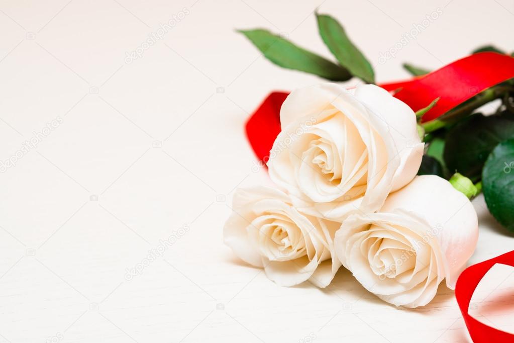 White roses with red ribbon on a light wooden background. Women'