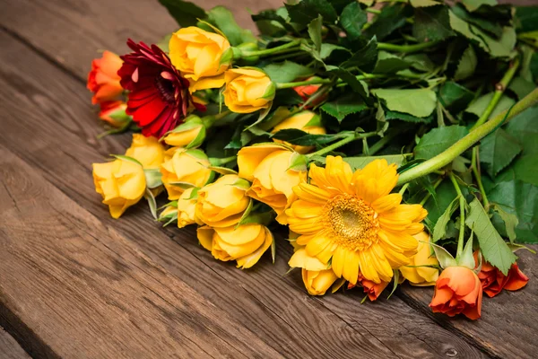 Yellow, orange roses and herberas on a wooden background. Women' — Stock fotografie