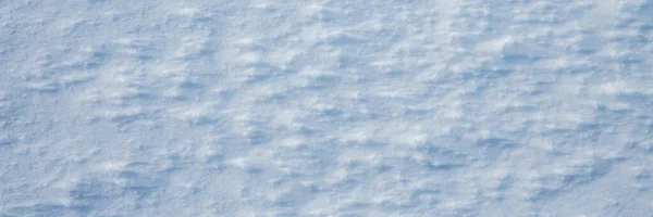 Natural snow texture. The surface of the snow crust. Snowy ground. Winter background with snow patterns. Closeup top view. Wide panoramic texture for background and design.