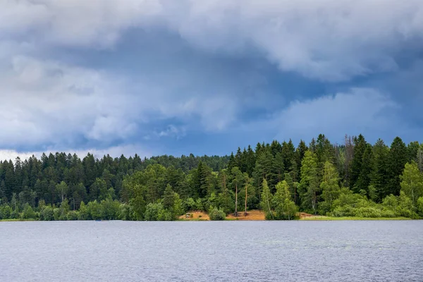 Picturesque lake landscape. There are dark clouds in the sky before the rain. View of the forest on the lake.
