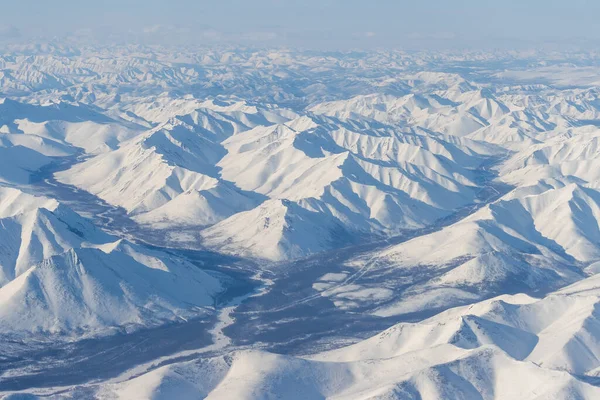 Aerial view of snow-capped mountains. Winter snowy mountain landscape. Air travel to the far North of Russia. Kolyma Mountains, Magadan Region, Siberia, Russian Far East. Great for the background.