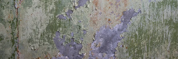 Peeling paint on the wall. Panorama of a concrete wall with old cracked flaking paint. Weathered rough painted surface with patterns of cracks and peeling. Grunge texture for wide panoramic background