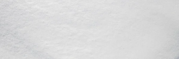 Beautiful winter background with snowy ground. Natural snow texture. Wind sculpted patterns on snow surface. Wide panoramic texture for background and design. Closeup top view with copy space.