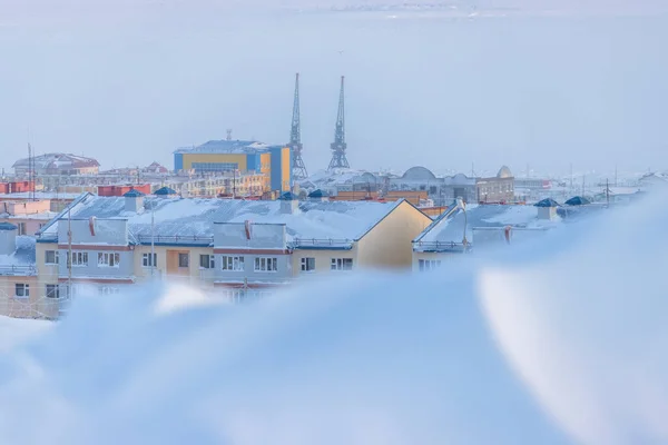Winter view of a snow-covered northern city in the Arctic. Roofs of buildings. Cold frosty winter weather. A lot of snow. Harbor cranes in the distance. Anadyr, Chukotka, Siberia, Far North of Russia.