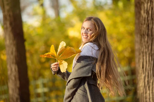 Autumn mood. Happy cheerful cute girl with yellow autumn leaves in her hands. Beautiful smiling young woman with light brown hair. Outdoor portrait in the park. Fall season.