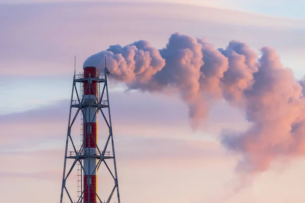 A chimney of a power plant and clouds of smoke, illuminated by red sunlight at sunrise. Aerial view of high smoke stack with smoke emission. Industrial zone, thick smoke plume. Industry and ecology.