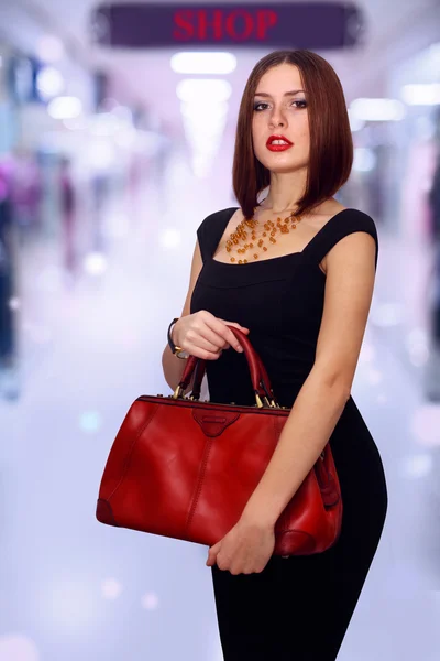 时尚性感的女人，拿在手中的红色皮革手提包姿势穿着优雅的黑色连衣裙 — 图库照片