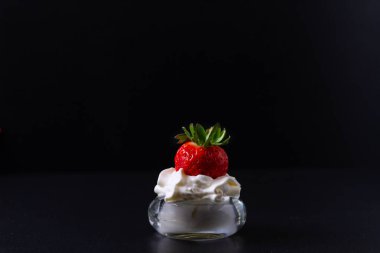 İçinde çırpılmış krema olan bir kaseye kısmen batırılmış çilek. Hepsinin siyah bir geçmişi var..