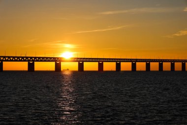 Şubat 2021 'de İsveç' in Limhamn kenti yakınlarındaki Öresund Köprüsü 'nün bir bölümünden güneşin batışı. Gökyüzü açık. Akşamları sütunların arasından görünen gemi.