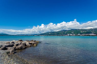 Gelendzhik Körfezi kıyısındaki taşlar. Güneşli bir gün. Arka planda dağlar ve beyaz kıvrımlı bulutlar.