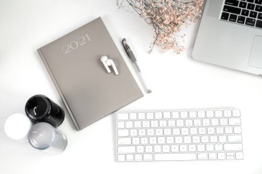 Bilgisayar, modern klavye, not defteri, kablosuz kulaklıklar, şık mumlar ve beyaz ofis masasında kurumuş çiçekler.