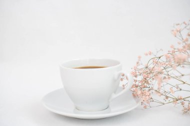 Beyaz bir masanın üzerinde bir fincan sade kahve ve kurumuş çiçekler.