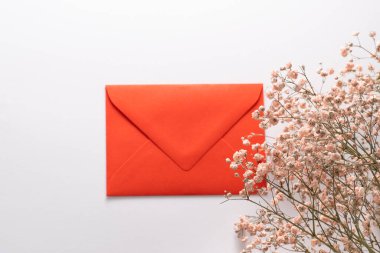 Beyaz arka planda kırmızı zarf ve bir buket kurutulmuş çiçek.