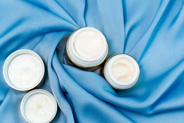 parlak mavi saten kumaş üzerinde altın rengi yüz bakım kremleri