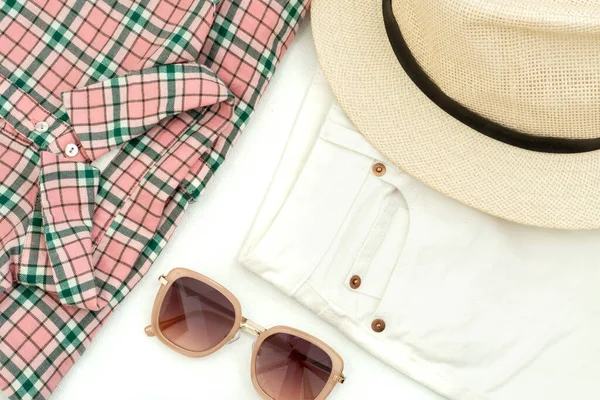 summer flat lay: shirt with a pink check pattern, sunglasses, white jeans and a woman\'s hat