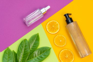 Kozmetik düz yatak: bronzlaştırıcı vücut parlatıcı kremi, yüz serumu ve doğal elementler arkaplan yeşil, mor ve sarı renklerin kombinasyonu