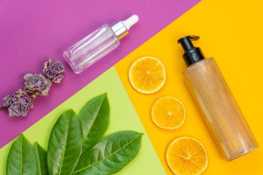 Kozmetik düz yatak: bronzlaştırıcı vücut parlatıcı kremi, yüz serumu ve doğal elementler arkaplan yeşil, mor ve sarı renklerin kombinasyonu