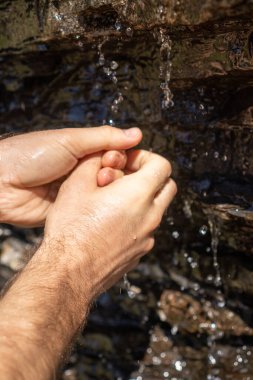 Bir adam ellerini İsviçre Alplerinde bir dağ deresinde yıkıyor.
