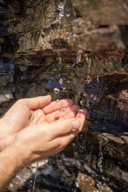 Bir adam ellerini İsviçre Alplerinde bir dağ deresinde yıkıyor.