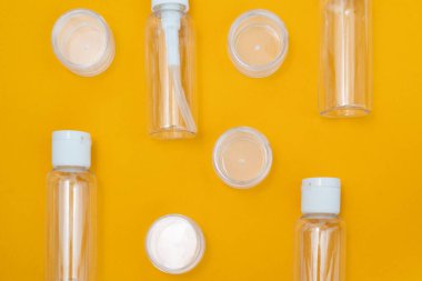 Sarı zemin üzerinde kozmetik ürünler için küçük gezici şişe ve kavanozların bileşimi