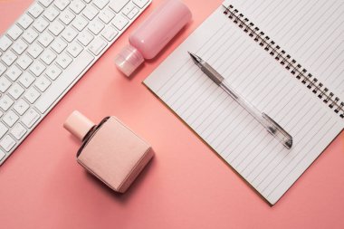 İş konsepti. İş aksesuarları ve kadın kozmetikleriyle çalışma alanı: pembe arka planda klavye, kalem, defter, parfüm ve kuru çiçekler 