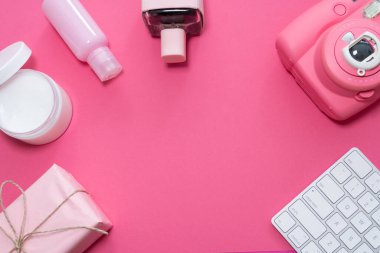 Üst kattaki ofis masası ve malzemeler. Çalışma masasının, klavyeli, kozmetik aksesuarlı ve pembe arka planda pembe hızlı baskı kameralı yaratıcı düz yatay fotoğrafı. 