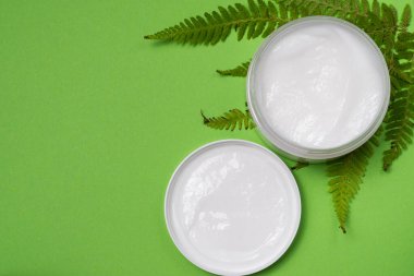 Yüz bakımı kozmetik ürünleri göz kremleri ve yeşil yapraklı düz kompozisyon yeşil arka planda