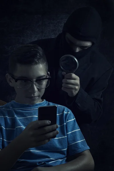 Человек в маске шпионит данные со смартфона подростка — стоковое фото