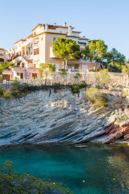 Lüks Düşük Yükselen Akdeniz Resort Oteli ya da Uçuruma Bakan Turkuaz Göl 'ün tepesine tüneyen ve Ilık Gün Batımında Parlak Güneş Işığıyla aydınlatılan Yeşil Ağaçlarla çevrili Tatil Evi