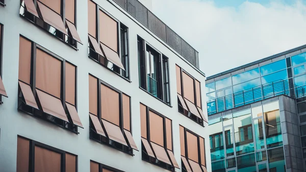 Geniş camlı ve güneşlikli iki modern bina çapraz uçaklar boyunca hizalanmış.