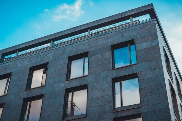 Mavi gökyüzü ve bulutlar apartman binasının camlarına yansıyor.