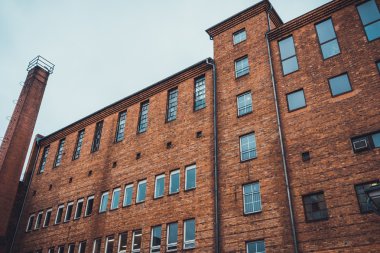 Endüstriyel binanın dış duvarı. Gökyüzünün altında kırmızı tuğlalardan yapılmış dikdörtgen bacası var.