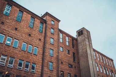 Dış duvarında beton asansör boşluğu olan endüstriyel tuğla binanın arka kısmının düşük açılı görüntüsü.