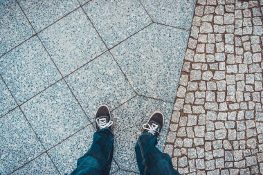 Birinci şahıs bakış açısı modern ve eski kaldırım taşlarının üzerinde duran kişinin bacakları ve ayakları.