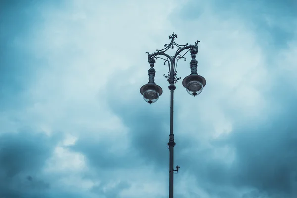 在阴云密布的蓝天下 由一根柱子上的两盏灯做成的老式铁制装饰性街灯 — 图库照片