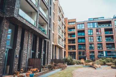 Modern ofis ya da apartman kompleksi olan farklı renklerdeki binalarla çevrili bir bahçe.