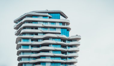 Modern apartman binası, her kattaki balkonların etrafını sürekli sarar. Kopya alanı olan gri gökyüzüne karşı.