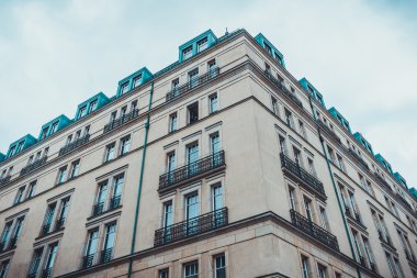 Bulutlu bir gökyüzünün altında mavi pencereli ve dekoratif balkonlu görkemli taş apartman manzarası