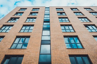 Kahverengi tuğlalı apartman kompleksinin düşük açılı görüntüsü. Mavi gökyüzünün altında, Almanya 'da beyaz kabarık bulutlu, sönük ışıklı pencereler var.