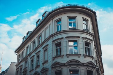Neoklasik binanın üst yarısında alçak açı manzarası eğri ön ve Fransız pencere camları ve mavi gökyüzü ve beyaz bulutların altında dormer pencereleri var.