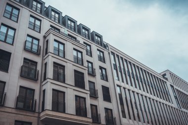 Bulutlu bir günde düz cepheli ve koyu renk pencereli modern apartman binalarının düşük açılı görüntüsü