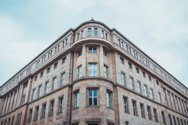 Açık kahverengi taş apartmanın alçak açılı manzarası. Yuvarlak köşeli, bulutlu bir gökyüzünün altında.