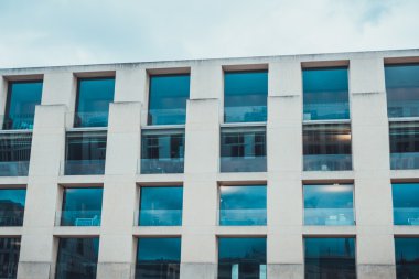 Kışın bulutlu bir gökyüzünün altındaki modern bir binanın dört sıra mavi renkli penceresini kapat.