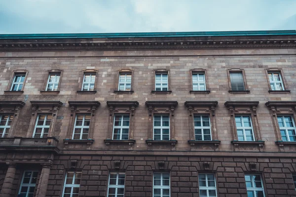 Street level view of brown stone apartment building with ornate windows and molding on a cloudy day in winter