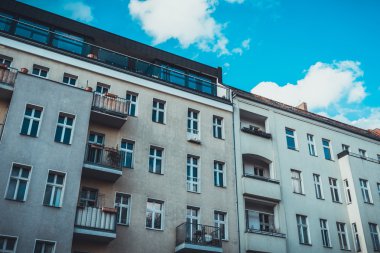 Kabarık bulutlu mavi gökyüzünün altında geniş pencereli ve geniş çatı katı stüdyosu olan büyük apartman kompleksinin dış görünüşü.