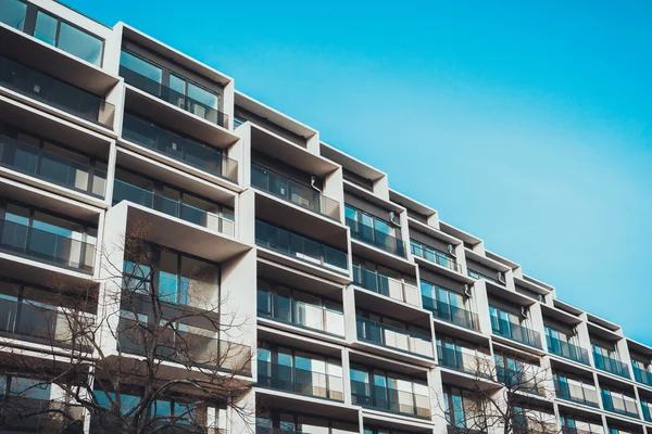 Açık mavi gökyüzünün altındaki çıplak dallı ağaçların arkasındaki balkonların alçak açılı görüntüsü