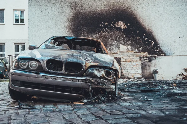 Yanıp kül olmuş lüks bir sedan, kavrulmuş, kapkara bir avluda. Aracın kararmış pencerelerinden içeriye yakın.