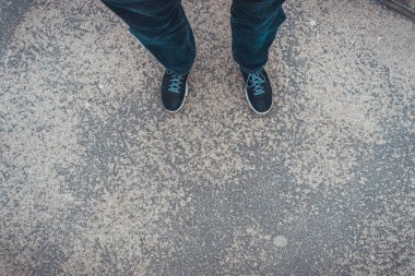 Spor ayakkabı ve kotla betonun üzerinde duran bir adamın ayaklarına bakmak, birinci şahıs bakış açısı.