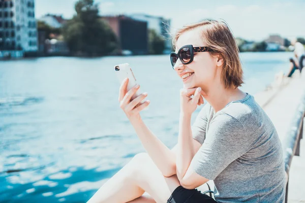 Gladlynt kvinna i solglasögon tittar på hennes telefon — Stockfoto