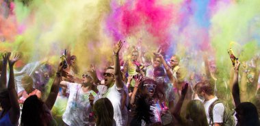 Geleneksel Holi kutlamaları sırasında etrafı pembe ve sarı duman ve tozla çevrili büyük bir grup mutlu insan.